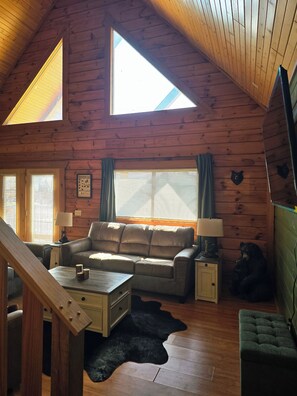 Ein Blockhaus-Interieur mit Schlafzimmer auf dem Dachboden, einer Couch, einem Couchtisch, einer Lampe und einer Bär-Dekoration.