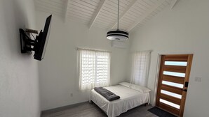 A bedroom with a bed, two windows with curtains, a ceiling fan, and a door.