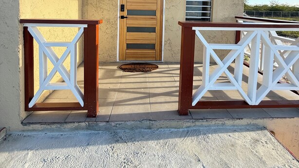 A covered outdoor area with a wooden door, a metal grill, and a white railing.