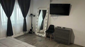 Ein Schlafzimmer mit einem Bett, einem Schminktisch mit Spiegel, einem Sessel, einer Kommode und einem an der Wand befestigten Fernseher.