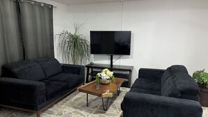 Ein Wohnzimmer mit zwei dunklen Sofas, einem Holztisch mit Blumenvase, einem Flachbildfernseher und einer großen Pflanze.