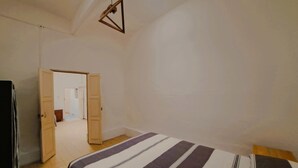 A bedroom with a bed, a door leading to another room, and a hanging light fixture.