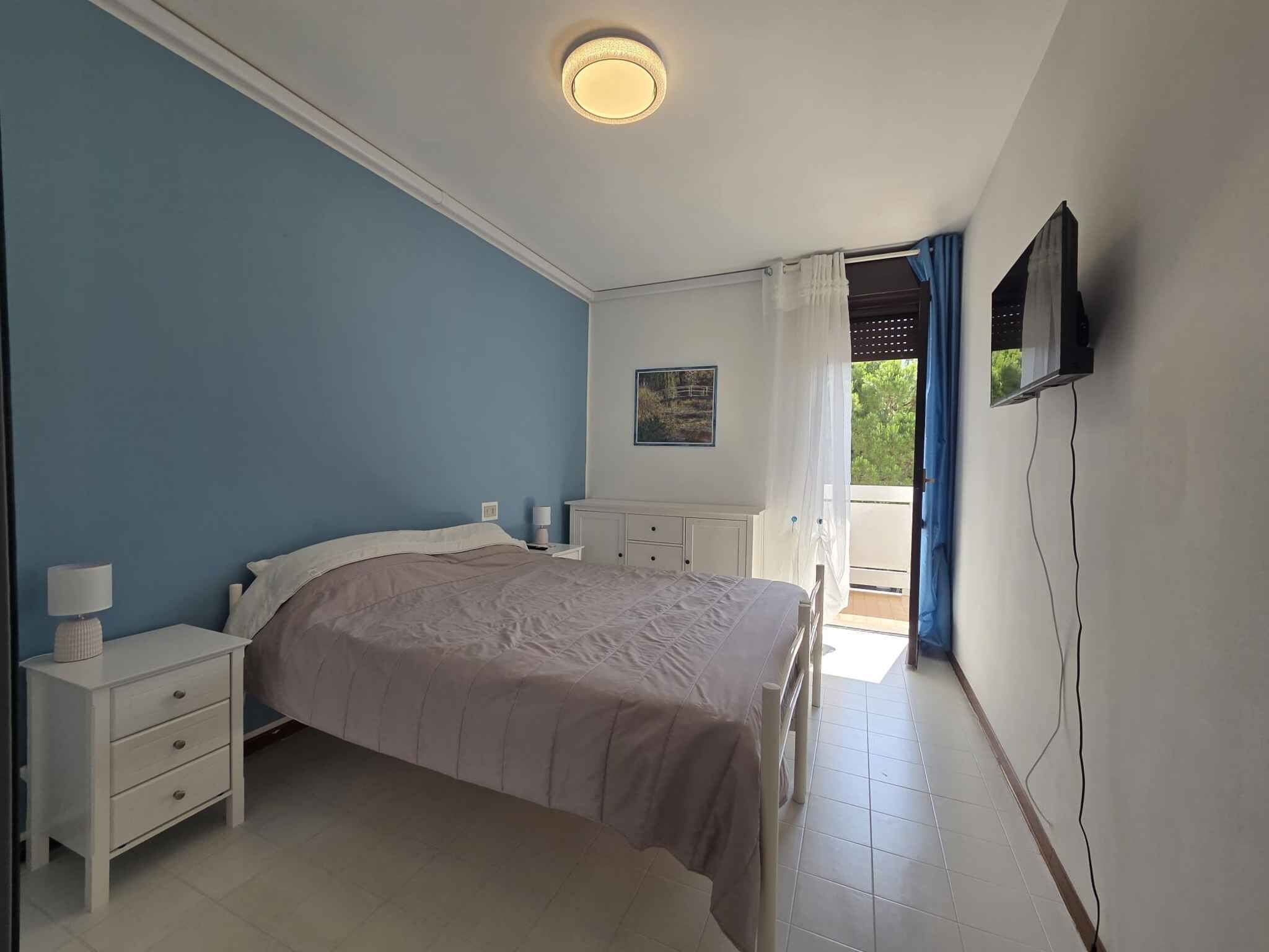 A bedroom with a bed, bedside tables, a TV, and a window with curtains.