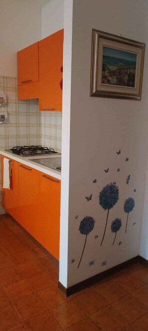 Eine Küche mit orangefarbenen Schränken, einem Gasherd und einer Wand mit einem gerahmten Bild.