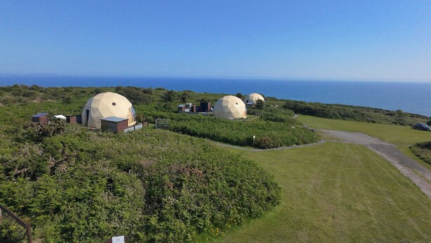Varias estructuras en forma de cúpula en un paisaje verde y exuberante, con vista despejada al mar.