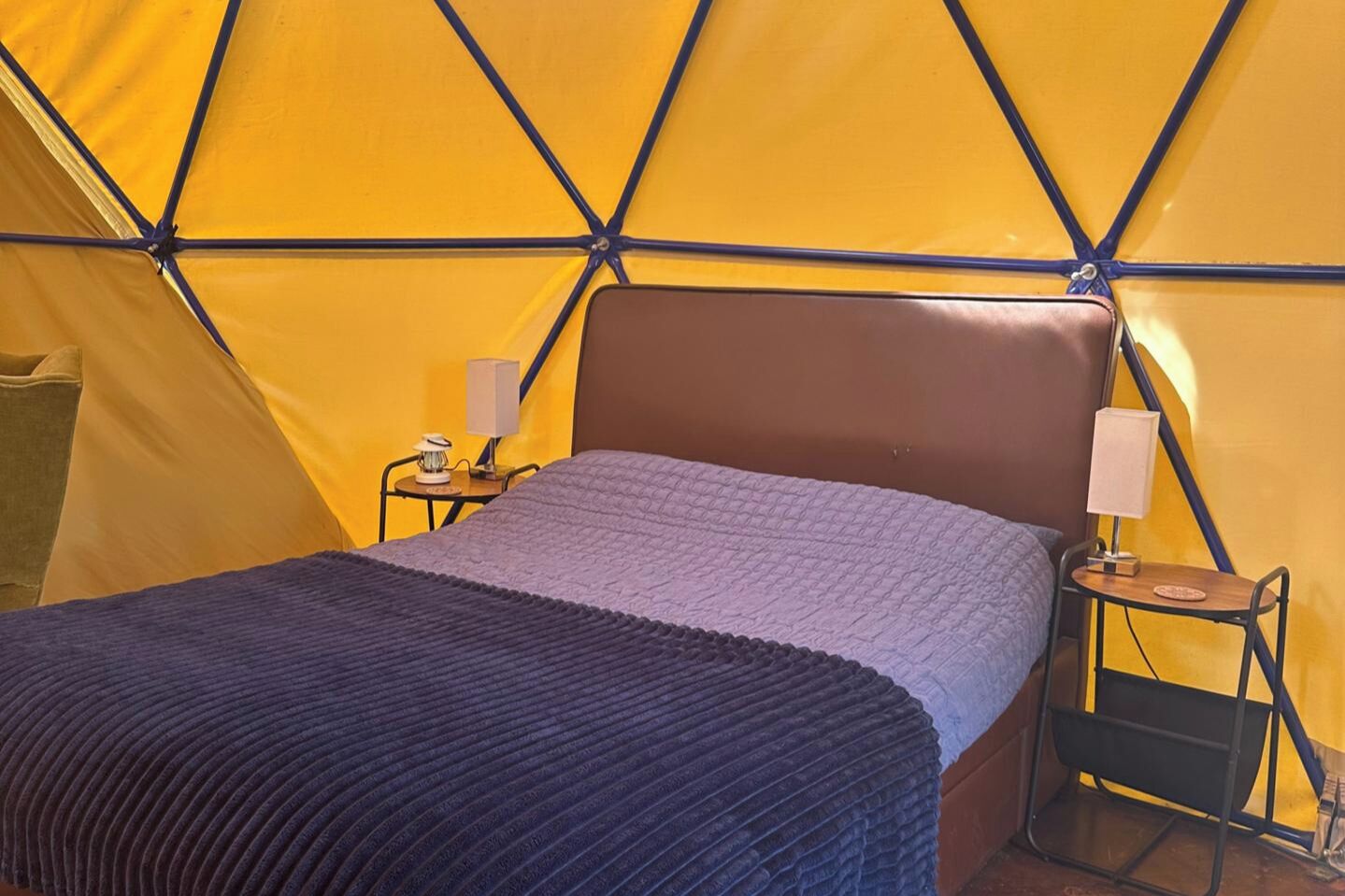 Une pièce aménagée comme une tente, avec un lit, deux tables de chevet et des lampes.