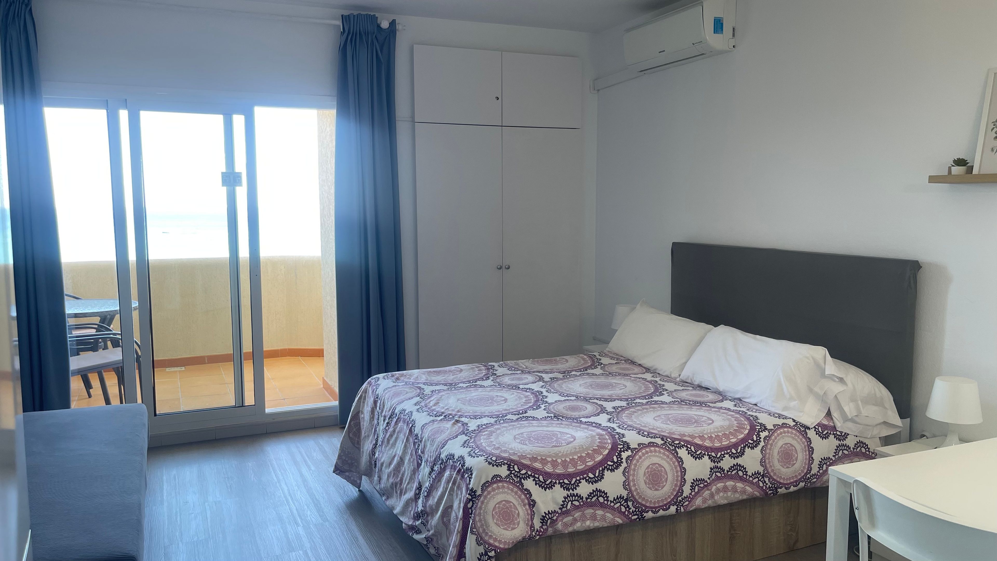 Habitación de hotel con cama, escritorio, silla, armario y balcón con mesa y sillas.