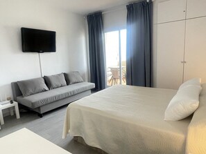 A hotel room with a bed, a sofa, a TV mounted on the wall, and a balcony with curtains. - Cozy Studio in Malaga with Extra Beds (Malaga)