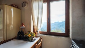 A kitchen with a window, a clock, a table with a lamp, and a vase with flowers. - Cozy Cottage Retreat in Berzi (Berzi)