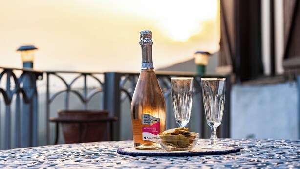 A bottle of Tenuta RIVIERO PROSECCO DOCG extra dry wine, two glasses, and a bowl of crackers on a table with a metal railing and a sunset in the background. - Cozy Cottage Retreat in Berzi (Berzi)