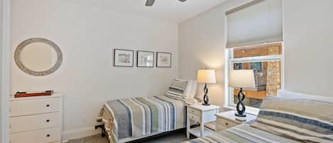 A bedroom with a bed, a nightstand, a lamp, a ceiling fan, a dresser, and a window with blinds.