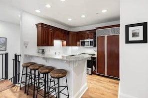 A kitchen with a central island, bar stools, wooden cabinets, a microwave, and a refrigerator. - Ballard Bliss - Modern, Comfortable 3BR/3BA (Telluride)