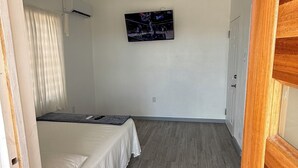 Un dormitori amb un llit, un televisor fixat a la paret, un ventilador de sostre i un terra de fusta.