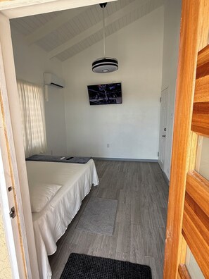 A room with two beds, a ceiling fan, a mounted TV, and a wooden floor. - Serenity Sunset (Codrington)