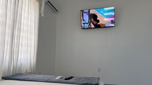 Un dormitori amb un llit, un comandament a distància i una televisió penjada a la paret.