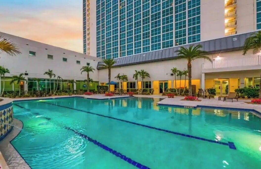 Ein Hotel mit Pool, Palmen und einem Hochhaus im Hintergrund.