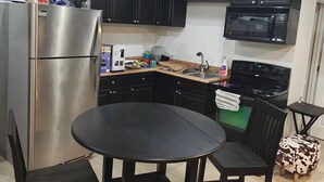 Una cocina con armarios oscuros, un refrigerador de acero inoxidable, un microondas, una estufa y una mesa redonda con sillas.