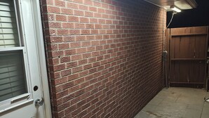 Pared de ladrillo junto a una puerta blanca con manija metálica, un portón de madera y un patio con baldosas.