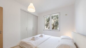 Un dormitorio con cama, cortinas blancas, una ventana y una lámpara colgante.