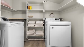 Une buanderie équipée de deux machines à laver, d’une étagère où sont pliées les serviettes et d’un panier à linge.