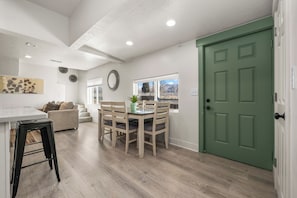 A modern kitchen with a dining table and chairs, a green door, and a view of mountains through a window.
