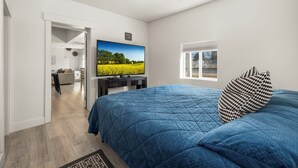 Une chambre à coucher avec un grand lit, une télévision, une fenêtre et une porte donnant sur une autre pièce.