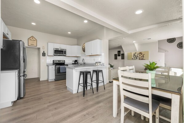 A modern kitchen with white cabinetry, a central island, bar stools, and a dining table with chairs.