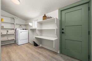 Une buanderie équipée d’un lave-linge, d’étagères et d’une porte verte.
