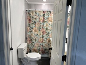 A bathroom with a toilet, a shower curtain with floral patterns, and a door with a handle. - Spacious 3-bedroom house close to Mid-America Industrial Park (Pryor)