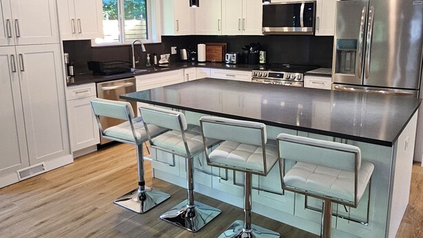 A modern kitchen with white cabinets, stainless steel appliances, and a central island with bar stools. - Halfmoon Bay Hideaway Top Suite (Halfmoon Bay)