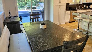 A modern kitchen with a wooden dining table, white benches, and a view of the outdoors. - Halfmoon Bay Hideaway Top Suite (Halfmoon Bay)