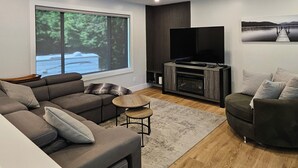 A modern living room with a sectional sofa, a small round table, a flat-screen TV, and a fireplace. - Halfmoon Bay Hideaway Top Suite (Halfmoon Bay)
