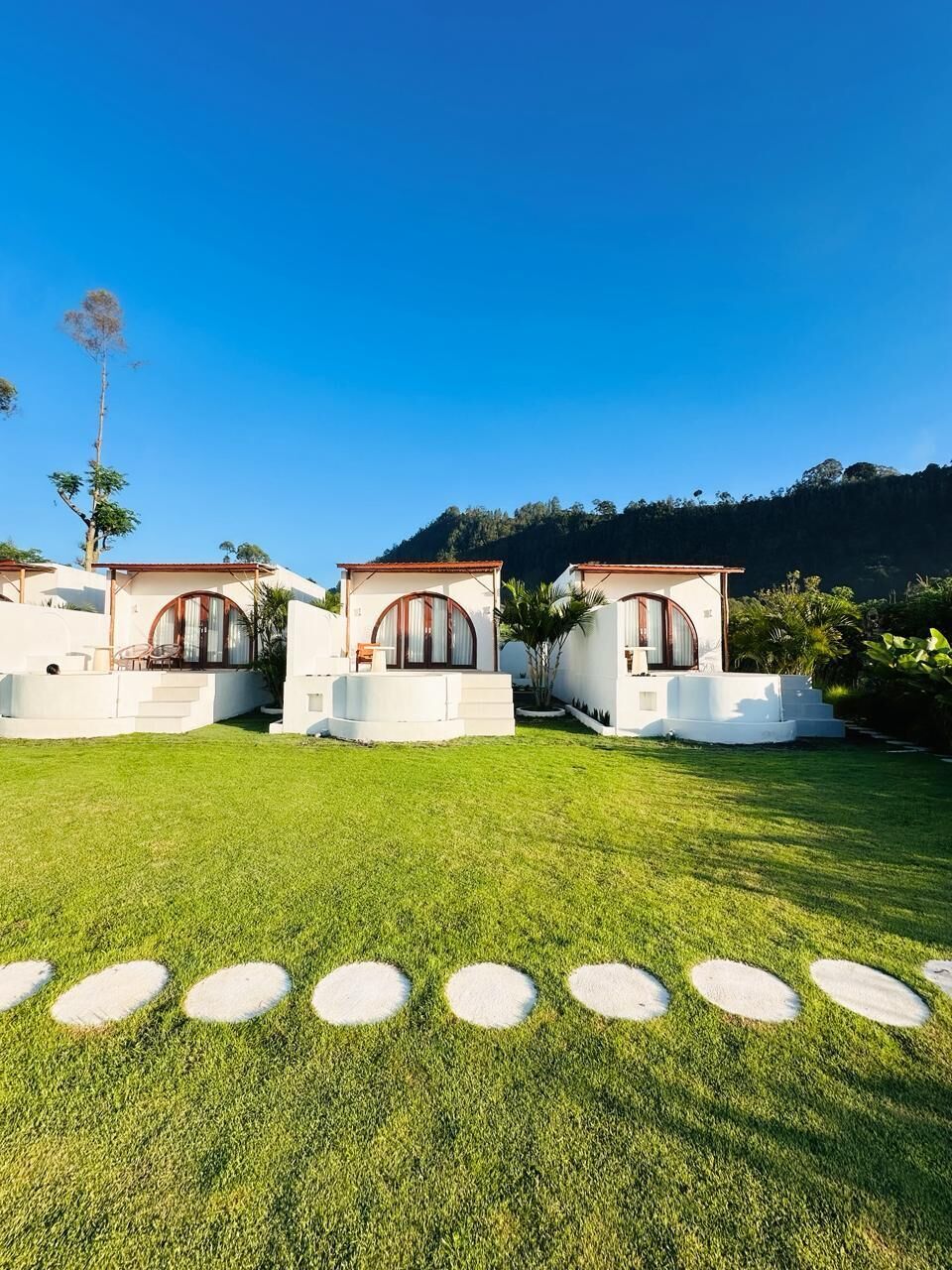 A property with three white buildings, each with a red roof and arched windows, surrounded by a well-maintained lawn and a clear blue sky.