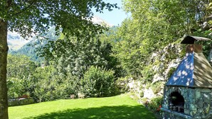 Eine steingebaute Außenkonstruktion mit Schornstein, umgeben von üppigem Grün und einer Rasenfläche.