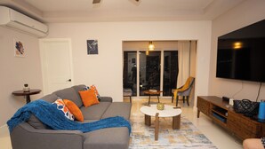 Una sala de estar con sofá, mesa de centro, televisor y puerta corrediza de vidrio que da a un balcón.