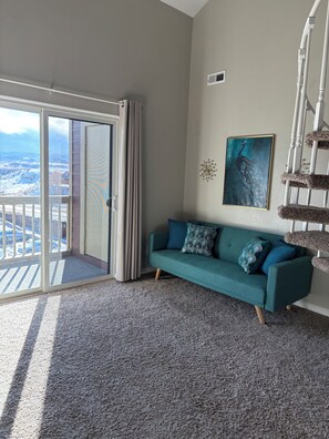 A room with a teal sofa, a painting, a cat tree, and a view through a glass door. - Spacious 2BR + loft, fully furnished, minutes to Red Rocks (Lakewood)