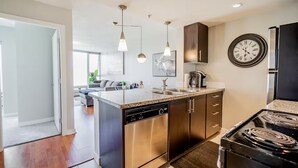 A modern kitchen with stainless steel appliances, a granite countertop, pendant lighting, and a clock on the wall. - 1BR Condo Near Rogers Arena | Heart of Vancouver (Vancouver)