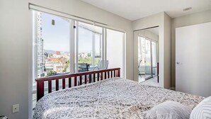 A bedroom with a large bed, a balcony with a view of the city, and a sliding glass door to a balcony. - 1BR Condo Near Rogers Arena | Heart of Vancouver (Vancouver)