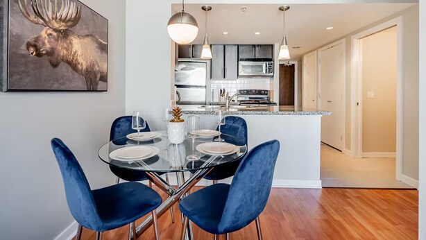 A dining area with a glass table, blue chairs, and a moose painting on the wall. - 1BR Condo Near Rogers Arena | Heart of Vancouver (Vancouver)