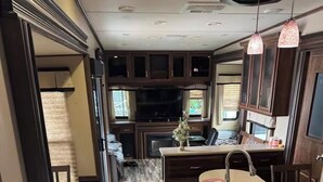 A compact RV kitchen with a built-in stove, a sink, and a dining area with a chair. - Cozy Backyard RV in Apopka/Orlando FL with AC (Apopka)