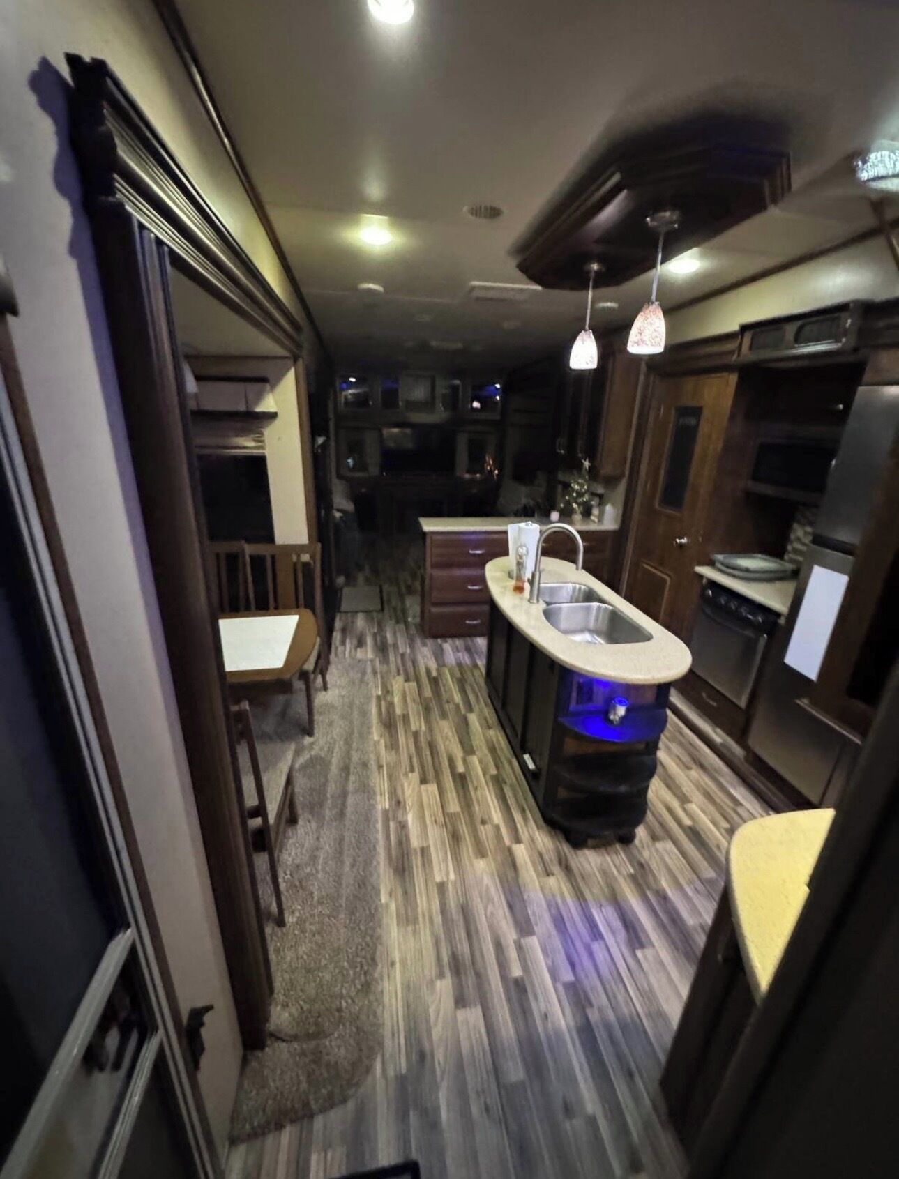 Una cocina estrecha con una isla central, piso de madera e iluminación colgante.