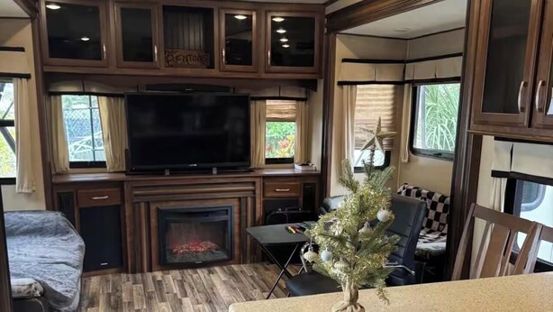 A well-lit RV interior with a TV, fireplace, dining area, and a small Christmas tree. - Cozy Backyard RV in Apopka/Orlando FL with AC (Apopka)