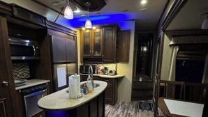 A modern kitchen with dark wood cabinets, a central island, and a dining area with a table and chairs. - Cozy Backyard RV in Apopka/Orlando FL with AC (Apopka)