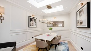 A modern dining room with a white table, beige chairs, a colorful rug, and a skylight. - Belgravia 4-bed House With Private Garden (London)