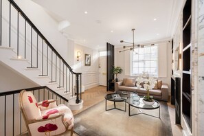 A spacious living room with a staircase, a sofa, a coffee table, and a fireplace. - Belgravia 4-bed House With Private Garden (London)