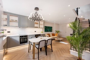 A modern kitchen with integrated appliances, a dining area with a chandelier, and a living space with a sofa and a plant. - Belgravia 4-bed House With Private Garden (London)