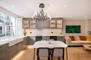 A modern kitchen with a dining area, a chandelier, and a sofa with cushions. - Belgravia 4-bed House With Private Garden (London)