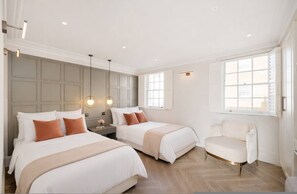 A hotel room with two beds, a sofa, a nightstand, and a window. - Belgravia 4-bed House With Private Garden (London)