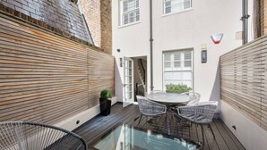 A patio with a glass table and chairs, a potted plant, and a door leading to an interior space. - Belgravia 4-bed House With Private Garden (London)