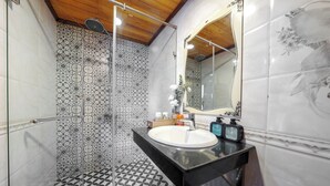 Un baño con suelo de baldosas estampadas, cabina de ducha con mampara de cristal, lavabo blanco con encimera negra y espejo con diseño floral.